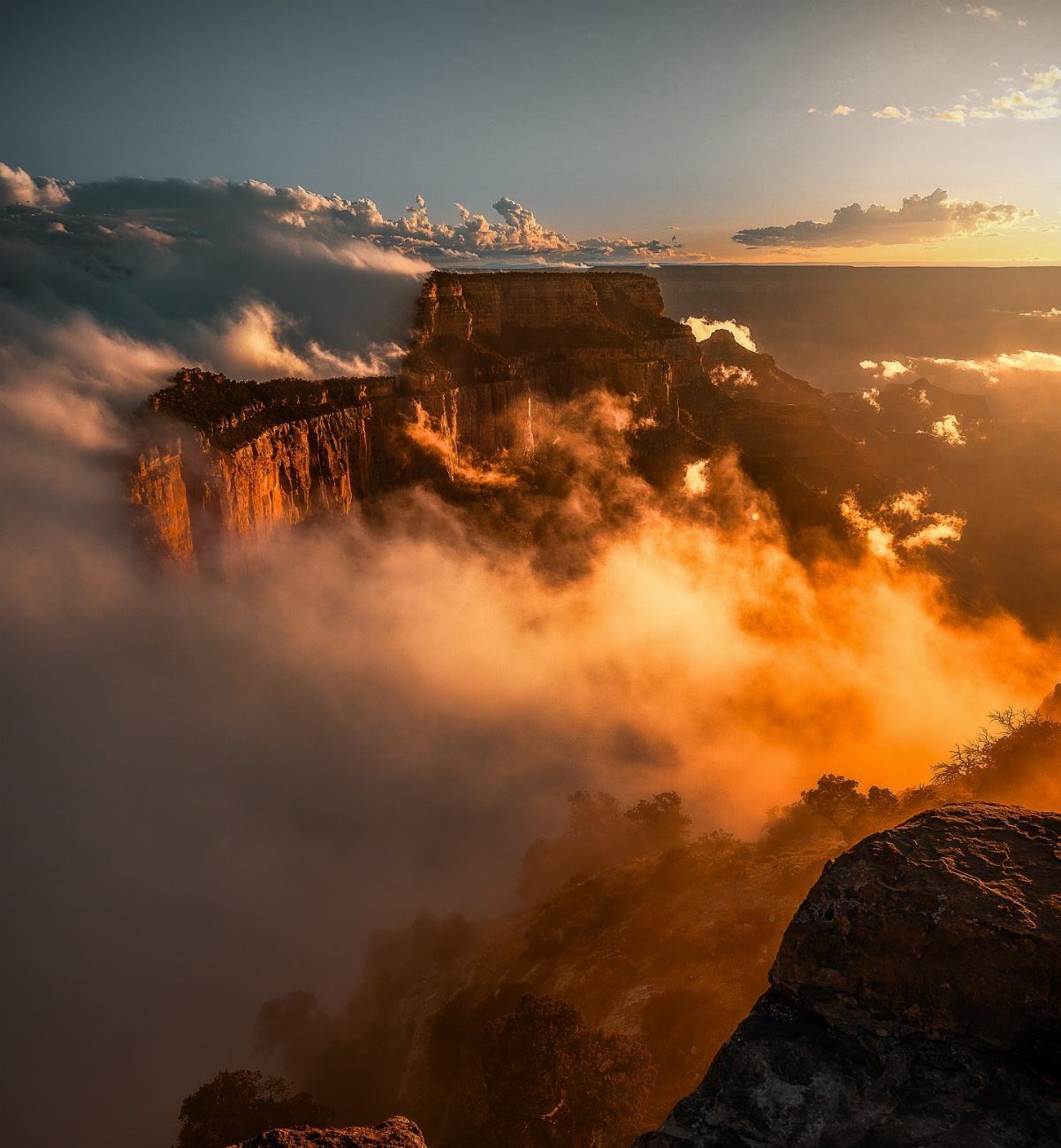 Steep orange canyon cliffs emerging from a sea of golden clouds at sunrise.