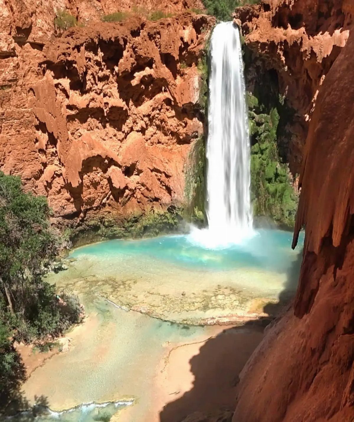 Waterfall cascading into a turquoise pool surrounded by red rock canyon walls