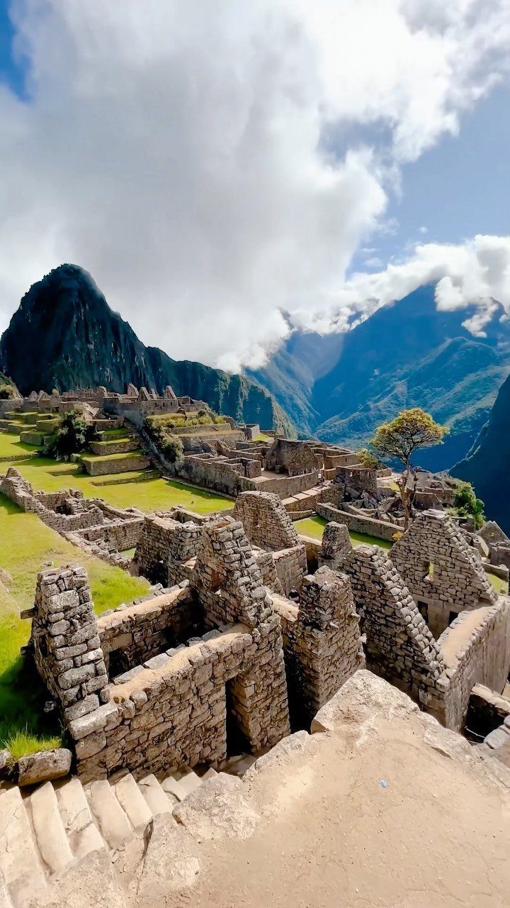 Ancient stone ruins and green terraces of Machu Picchu under a cloudy sky.