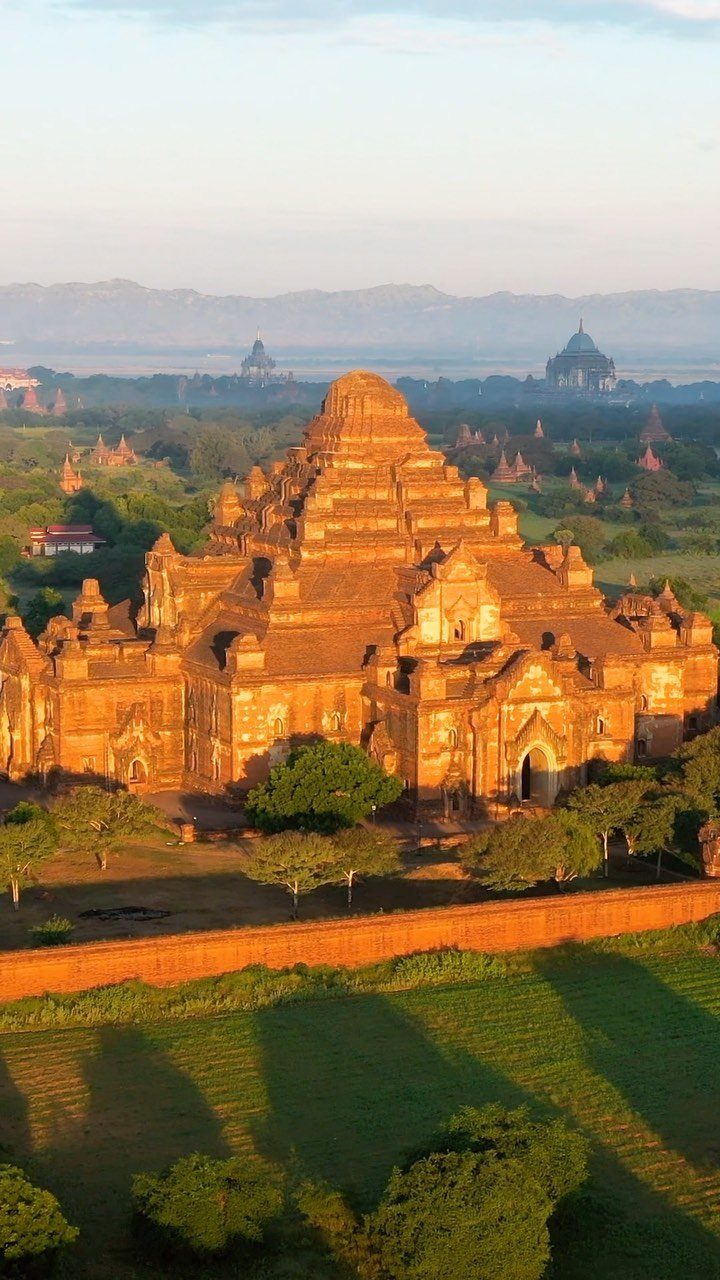 Ancient tiered brick pagoda surrounded by lush greenery under a soft morning sky.
