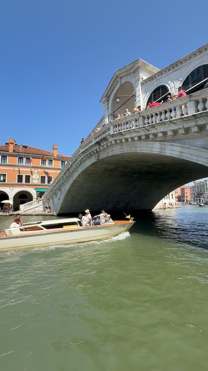 White stone bridge over a green canal with a motorboat and orange buildings.