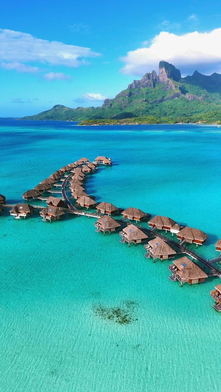 Overwater bungalows in a turquoise lagoon with a green mountain in the background.