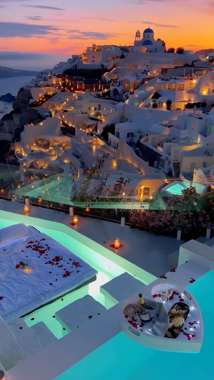 Whitewashed cliffside buildings and blue domes under a sunset sky with luxury terrace.