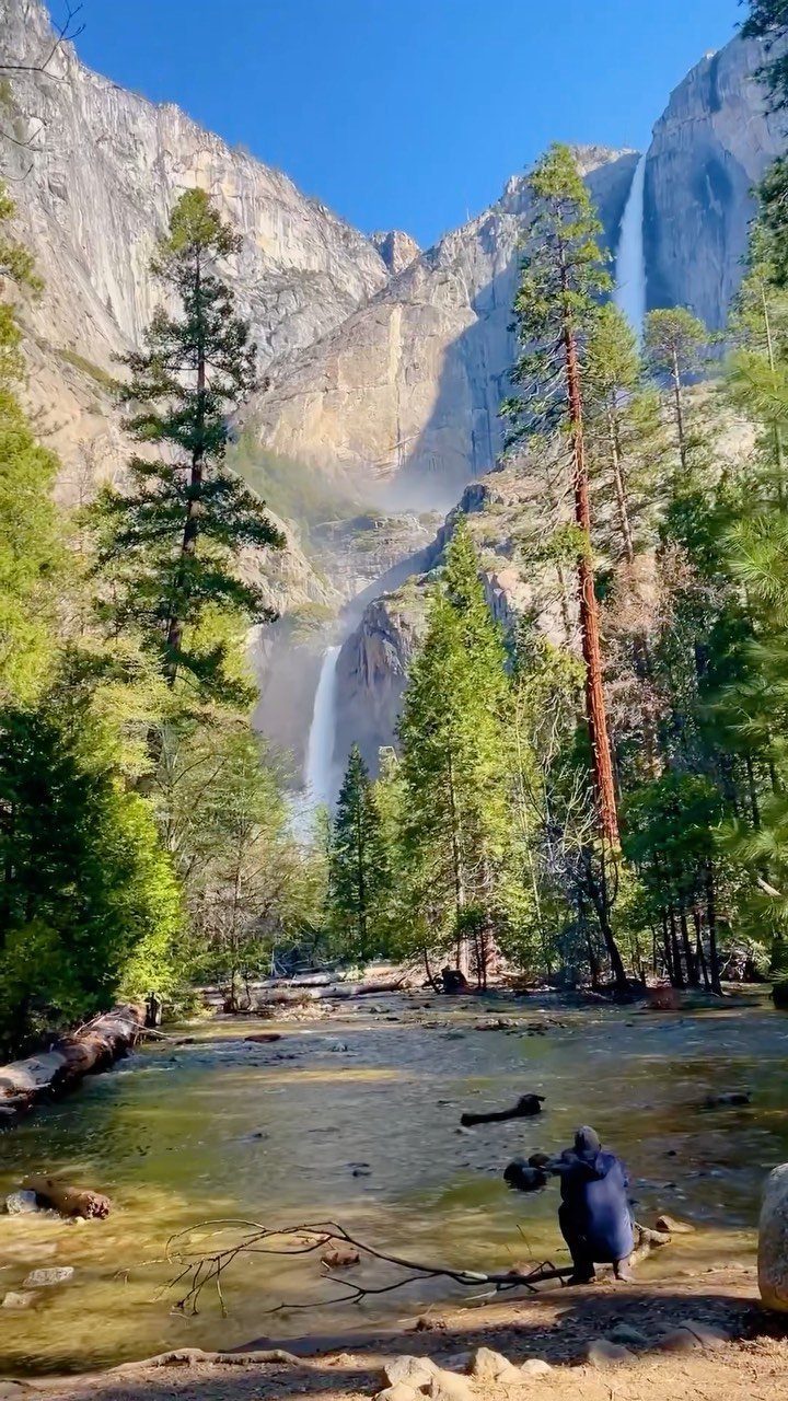 Granite cliffs and waterfalls in a lush valley with a river and pine trees.
