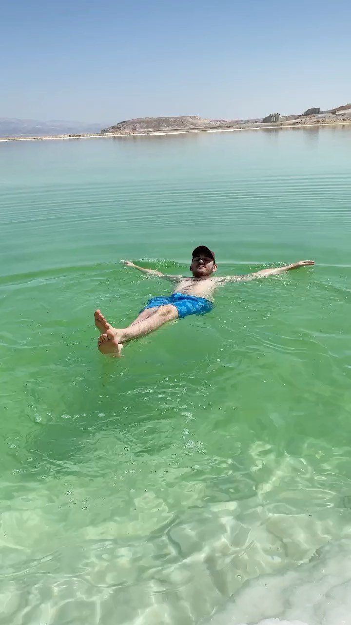 Man floating on his back in turquoise mineral waters with arid mountains behind.