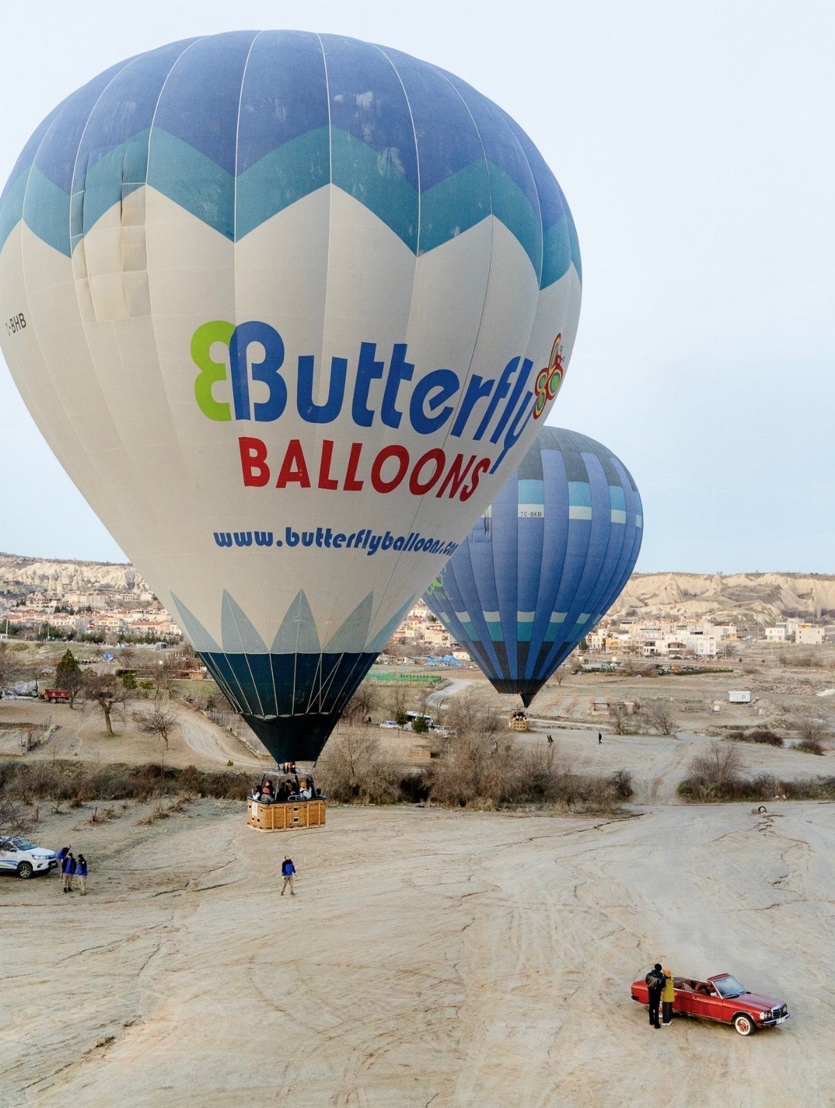 Two hot air balloons floating over a sandy landscape with distant hills.