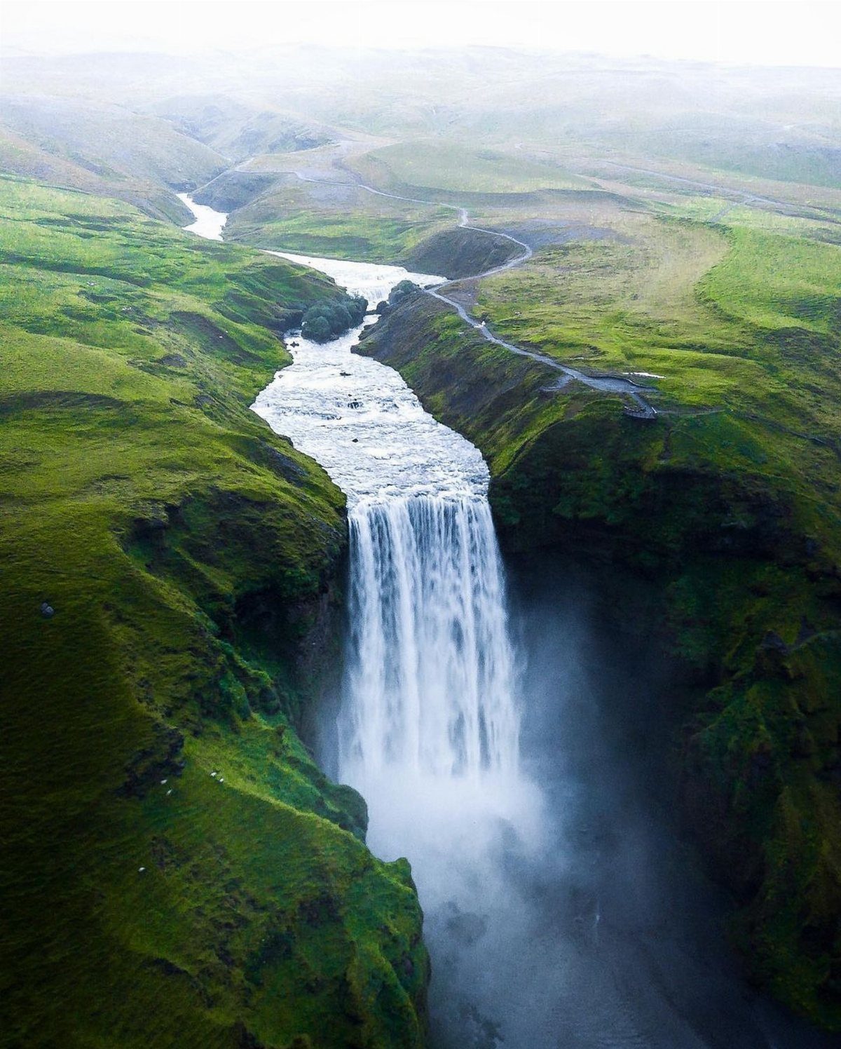 Large waterfall cascading into a gorge surrounded by lush green Icelandic hills