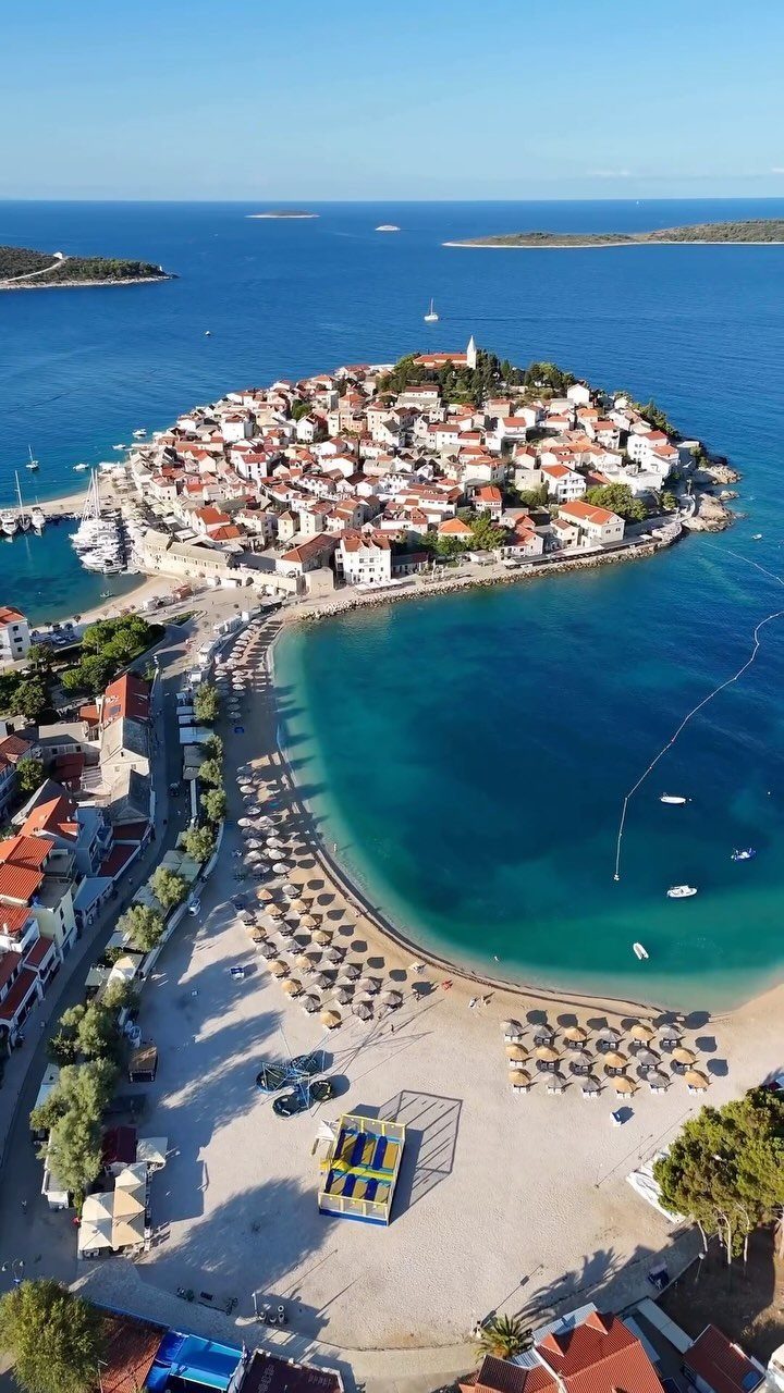 Coastal town with red roofs on a peninsula surrounded by turquoise Mediterranean waters.