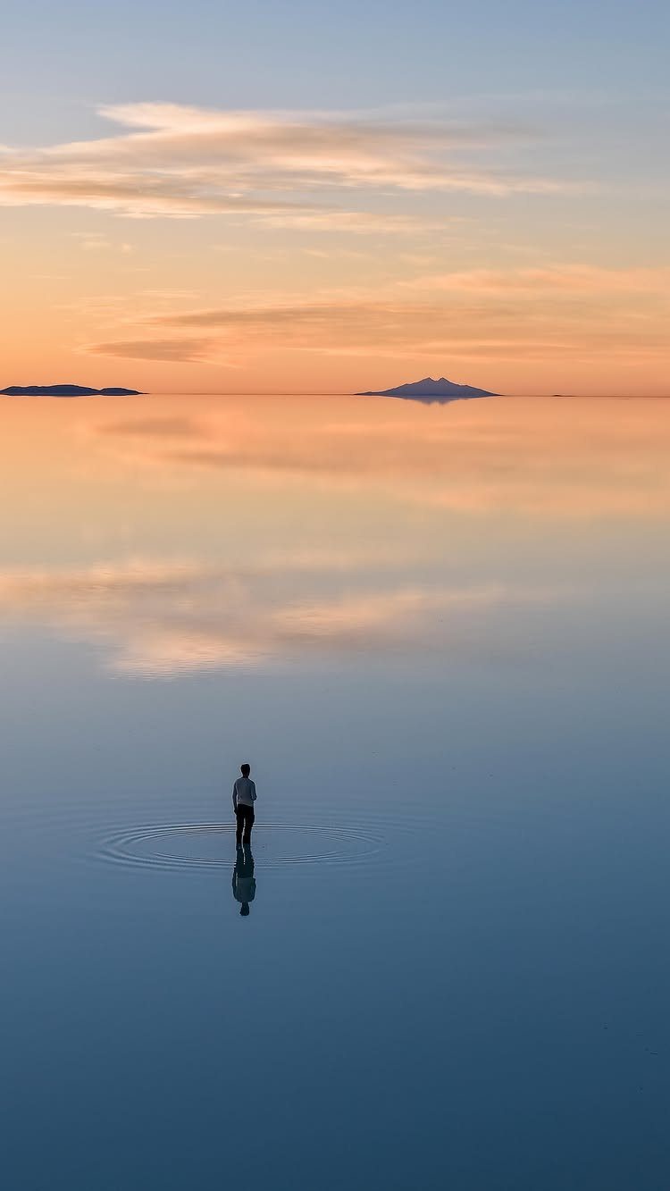 Person standing in shallow water with a perfect mirror reflection of the sunset sky.
