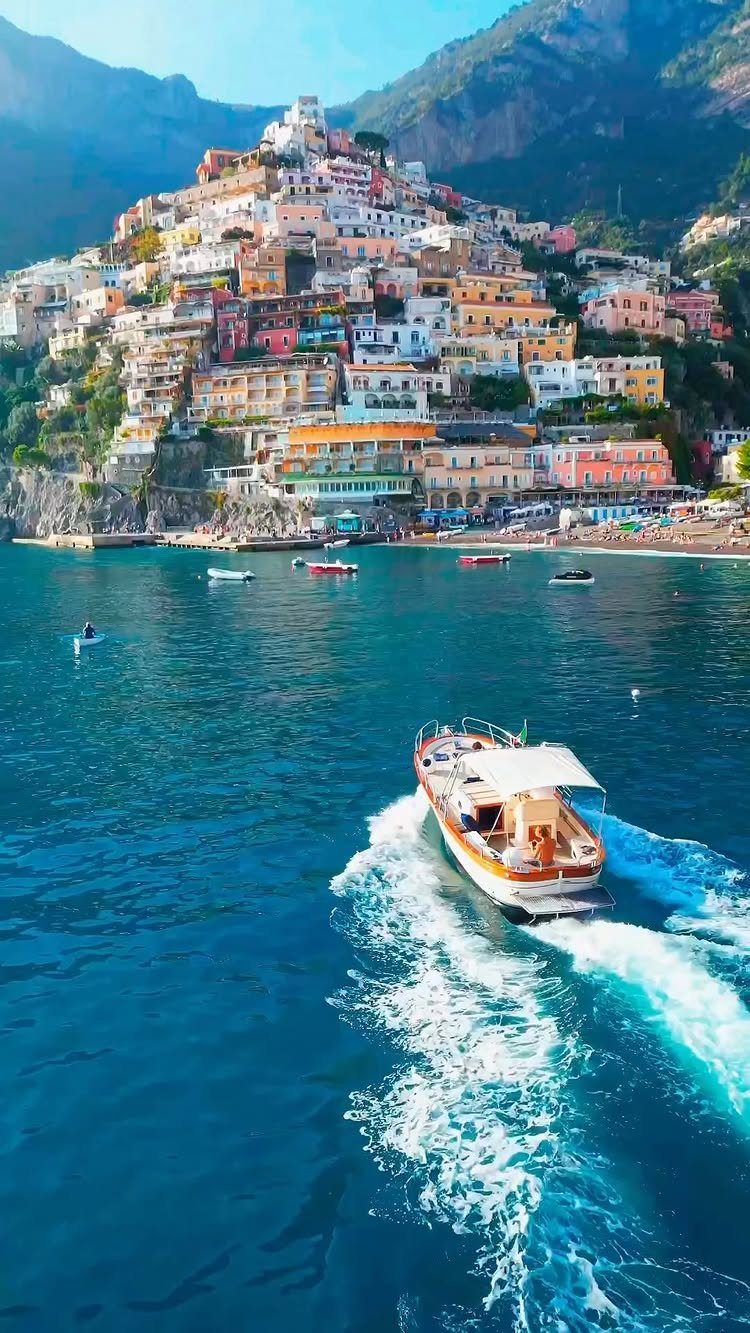 Colorful cliffside village overlooking a blue sea with a motorboat in the foreground.