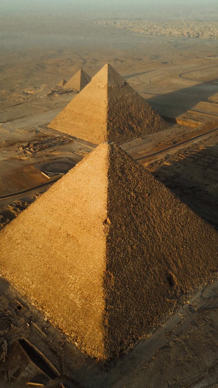Three ancient stone pyramids standing in a vast, sandy Egyptian desert landscape.