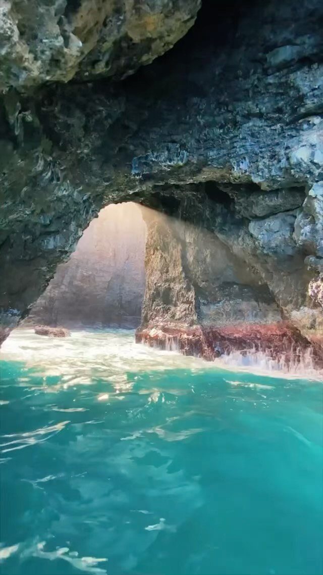 Turquoise ocean water inside a rocky sea cave looking out toward bright sunlight.