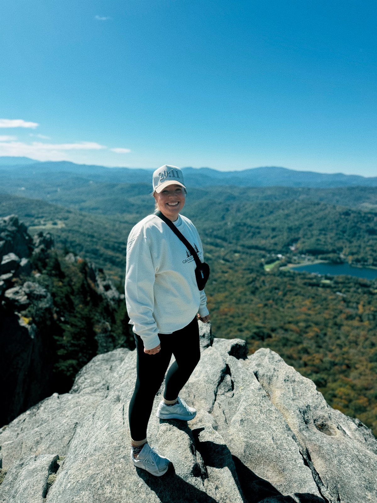 12 November Trip Ideas for Warm Beaches and Fall Color 2 Woman standing on a rocky mountain peak overlooking autumn forests and a lake.