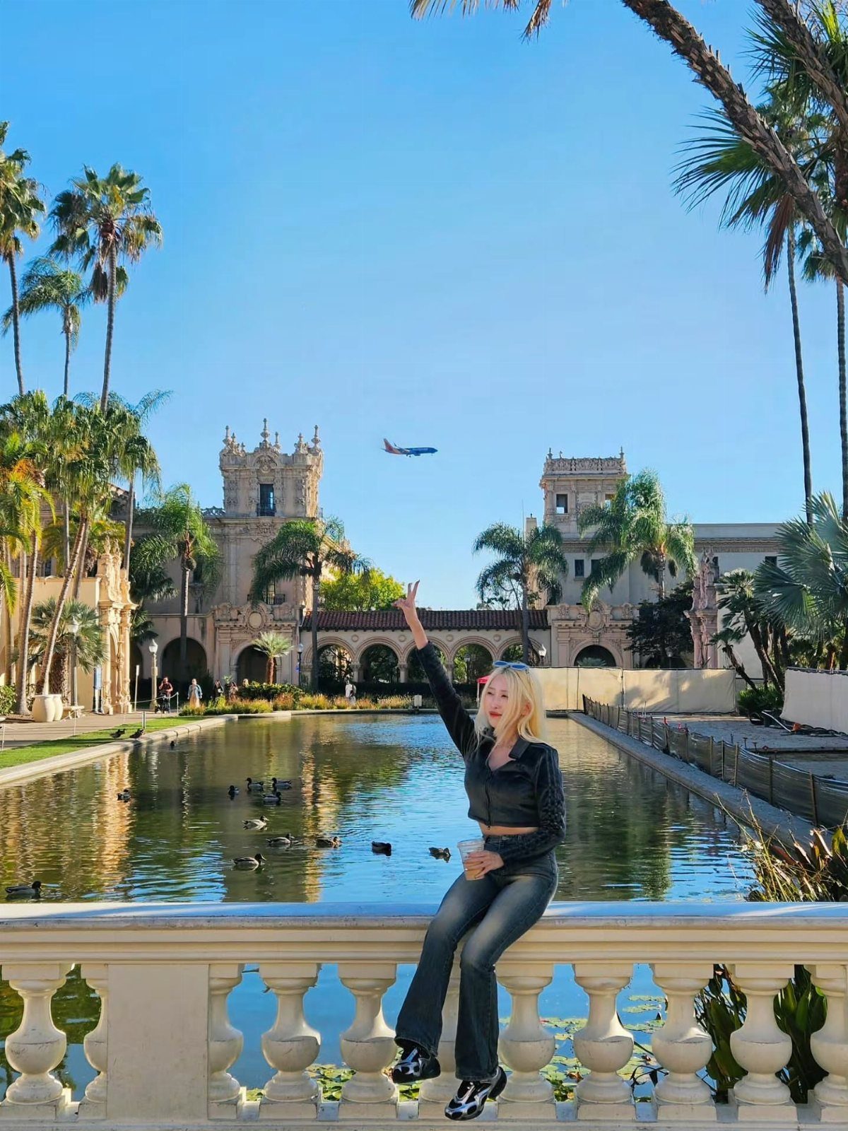 12 November Trip Ideas for Warm Beaches and Fall Color 10 Woman sitting on a stone railing before a grand Spanish-style building and pond.