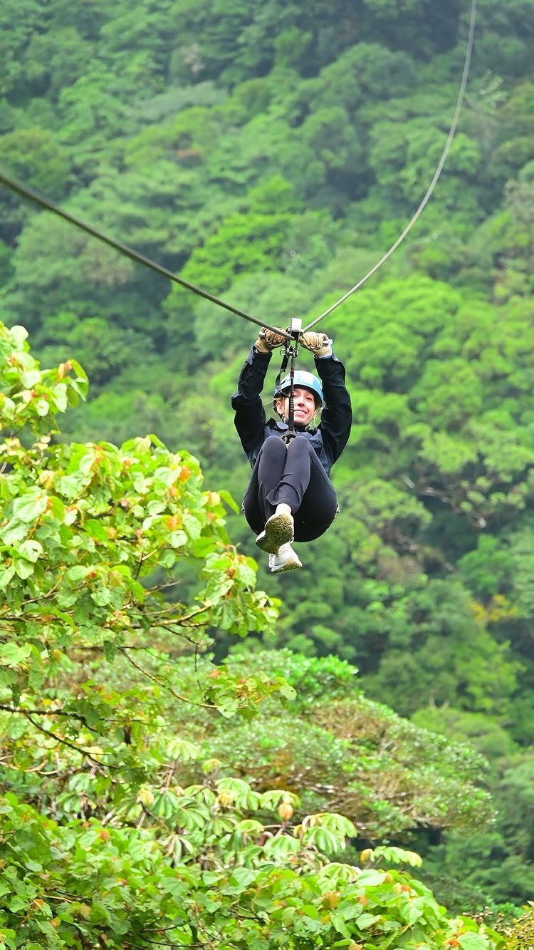 12 November Trip Ideas for Warm Beaches and Fall Color 6 Person zip-lining through a dense, green tropical forest canopy wearing a safety helmet.