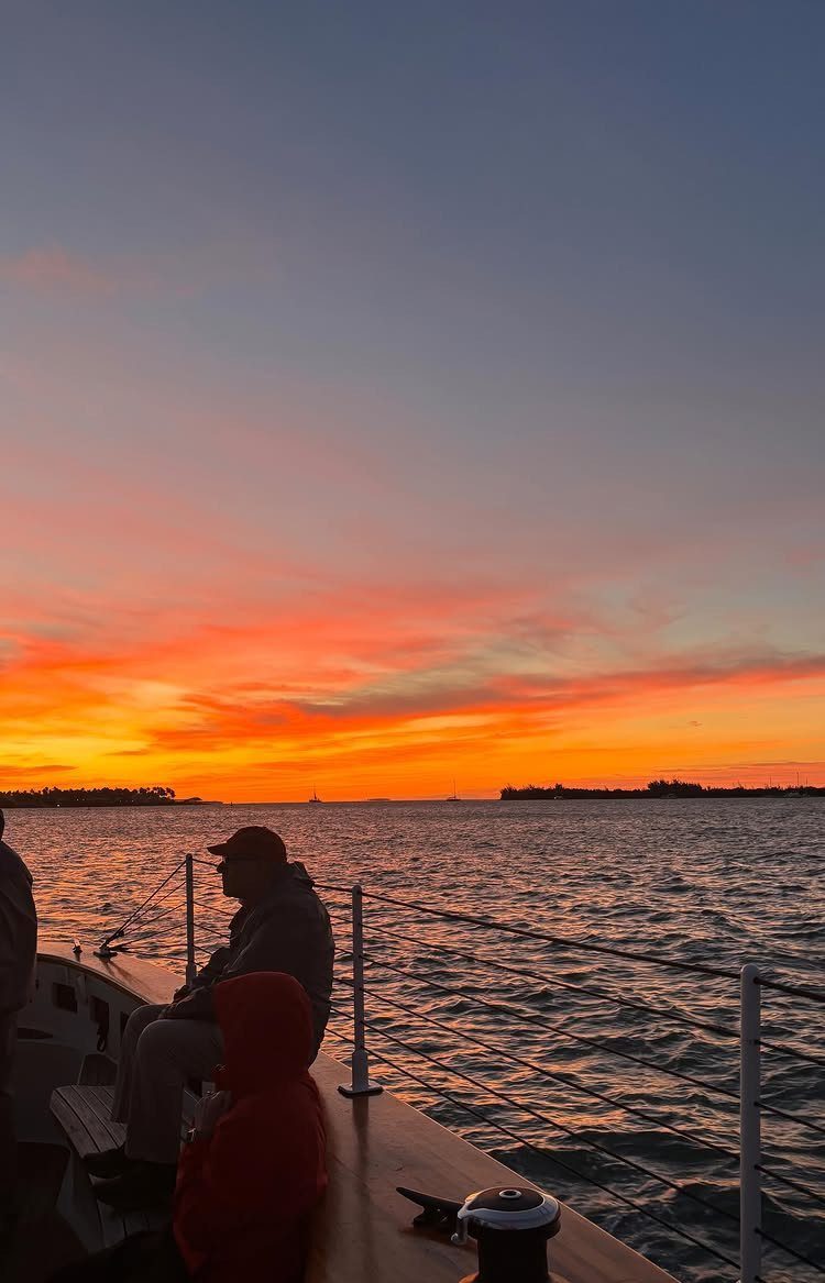 12 November Trip Ideas for Warm Beaches and Fall Color 11 People on a boat deck watching a vibrant orange and red sunset over water.