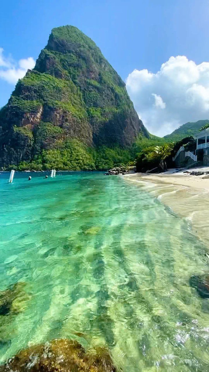 12 Places Like Bora Bora for Island Views and Lagoons 6 Green volcanic mountain peak overlooking a white sand beach and turquoise ocean water.