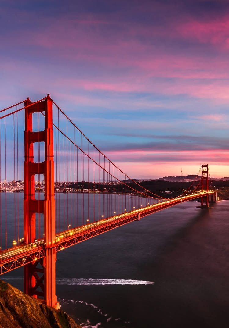 Golden Gate Bridge spanning water under a vibrant purple and pink sunset sky.