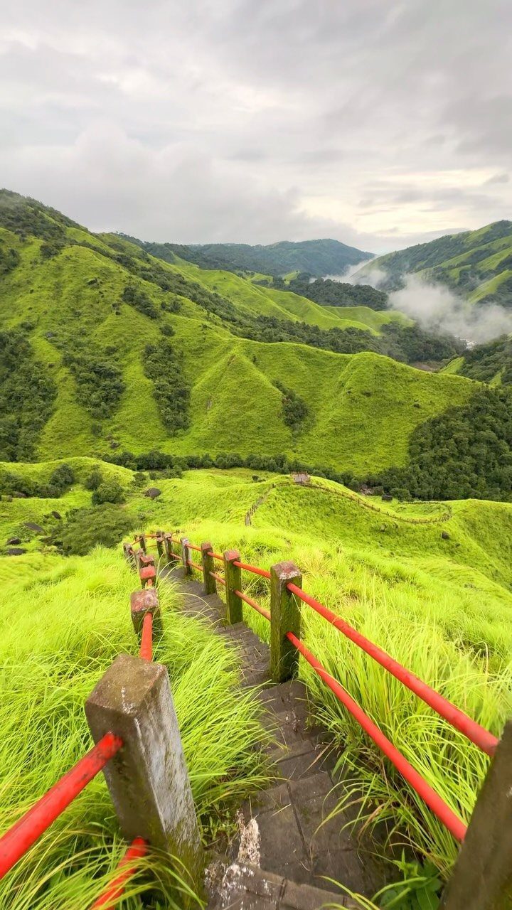 Stone stairs with red railings descending into a lush green mountain valley.