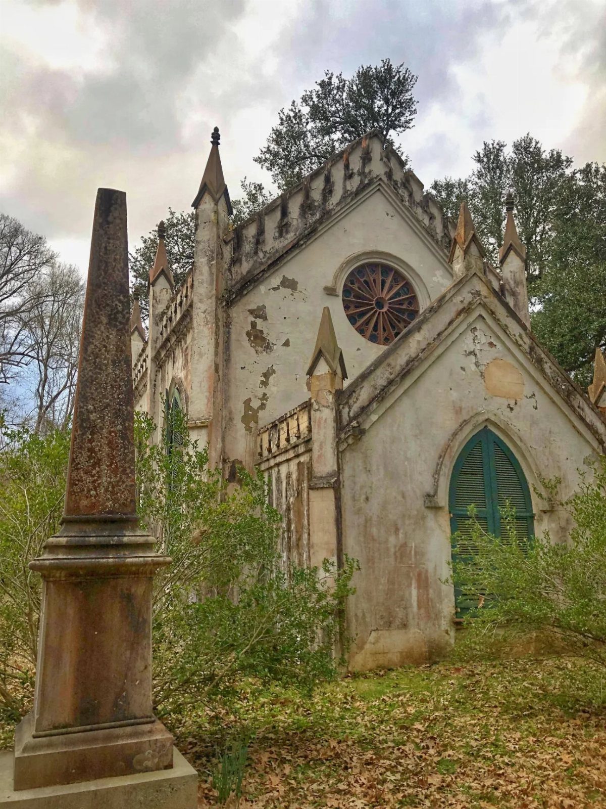 Weathered white stone mausoleum and obelisk surrounded by overgrown greenery and autumn leaves.