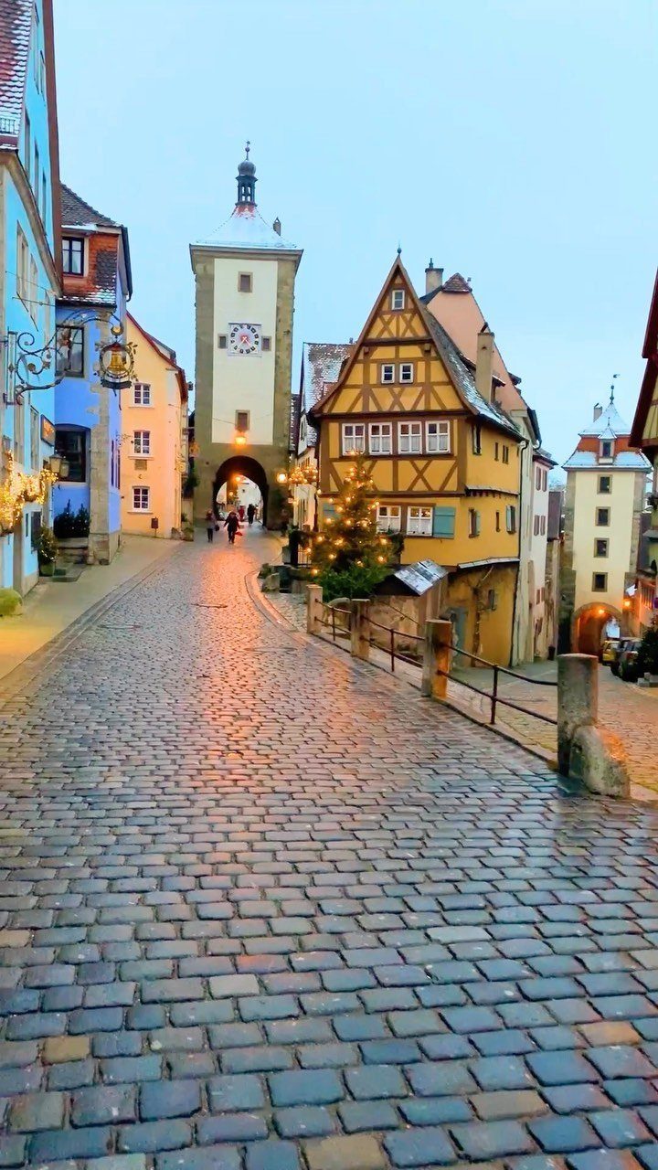 Cobblestone street with colorful half-timbered houses and a white clock tower in Europe.