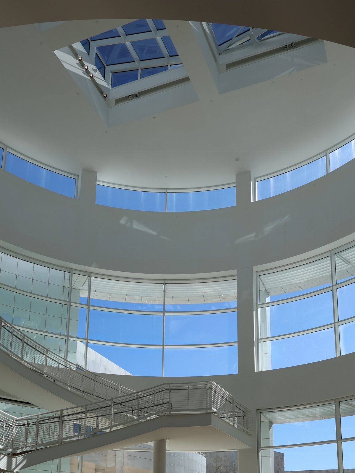 Modern white building interior with large windows, a staircase, and a ceiling skylight.