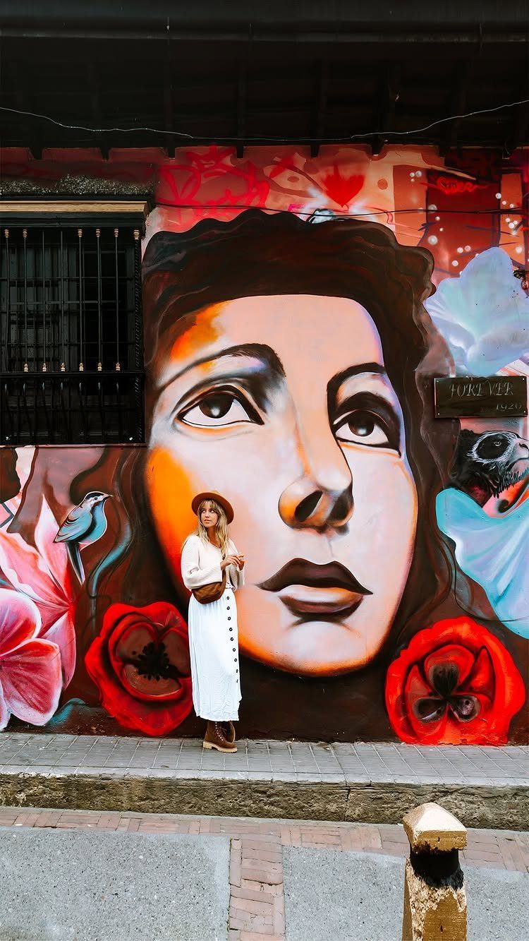 Woman in white dress posing before a colorful urban mural of a face.
