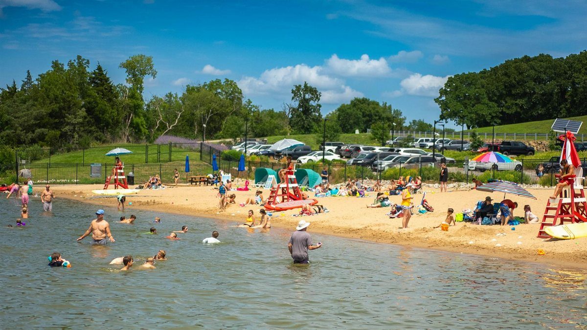 People swimming and relaxing on a sandy beach with a lifeguard stand nearby.