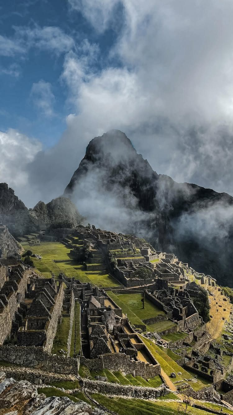 Ancient stone ruins and green terraces on a mountain under a cloudy sky.