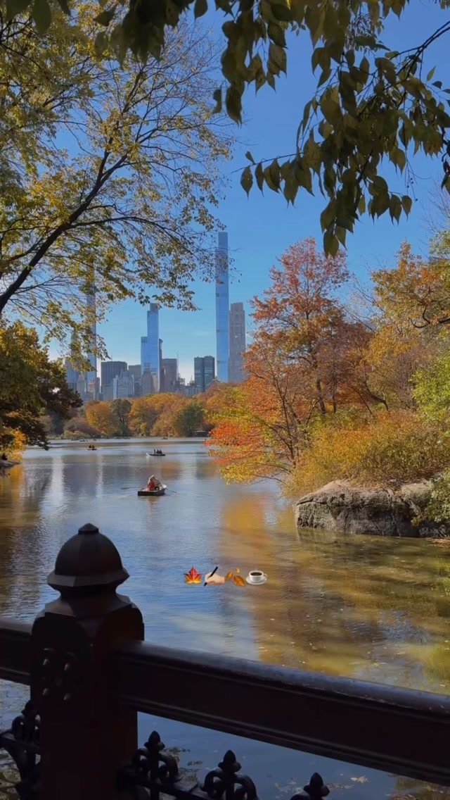Lake with autumn trees and a city skyline in the background under blue sky