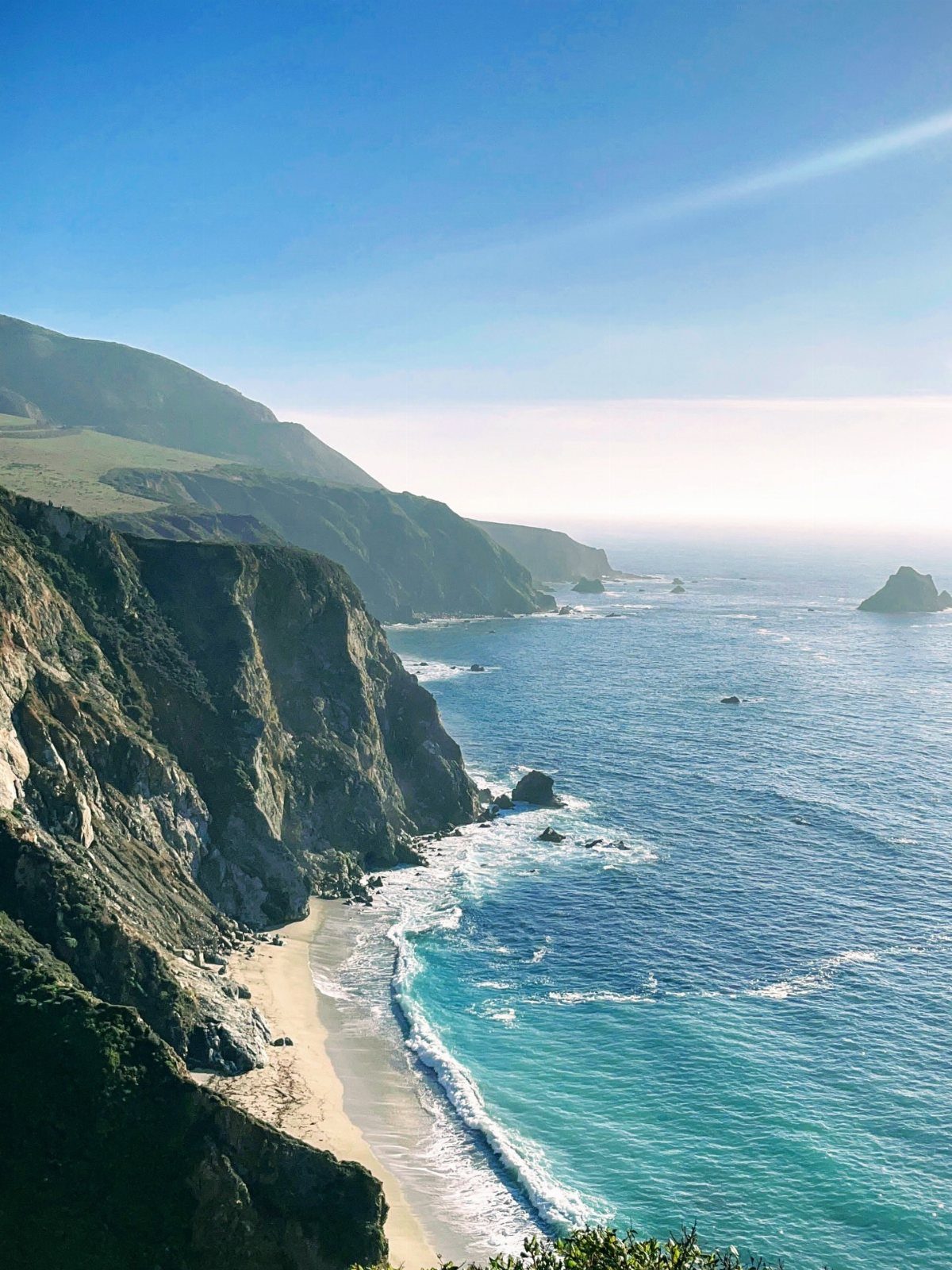Rugged coastline with steep cliffs, a sandy beach, and turquoise ocean water.