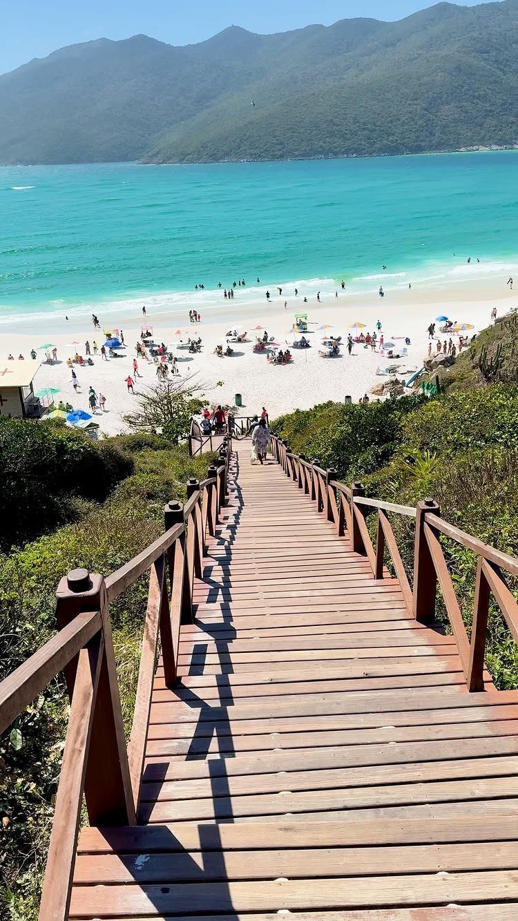 Wooden boardwalk leading down to a crowded tropical beach with turquoise ocean water.