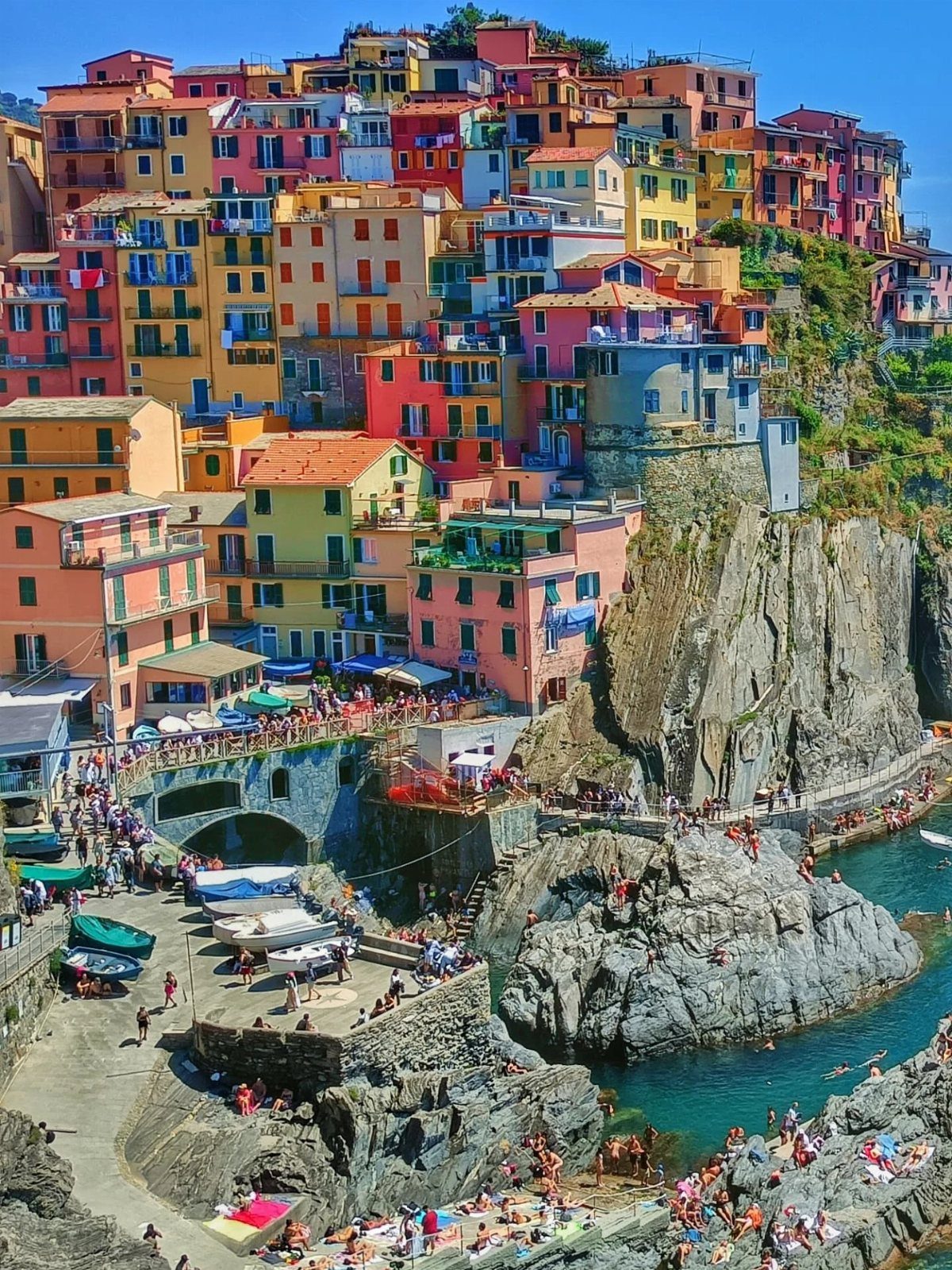 Colorful coastal village buildings perched on a rocky cliff above a turquoise bay.