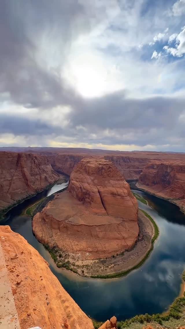 Horseshoe Bend river curving around red sandstone cliffs under a cloudy sky