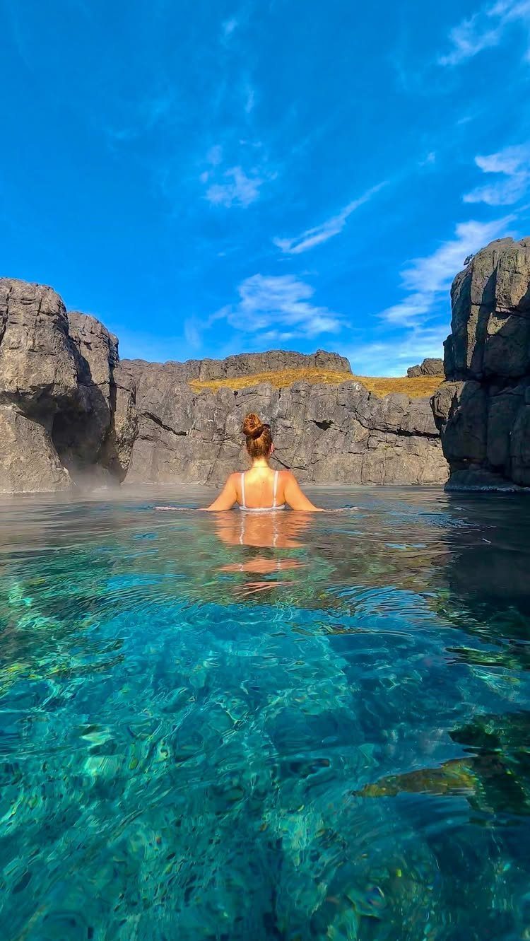 Woman soaking in a turquoise geothermal pool surrounded by dark volcanic rock formations.
