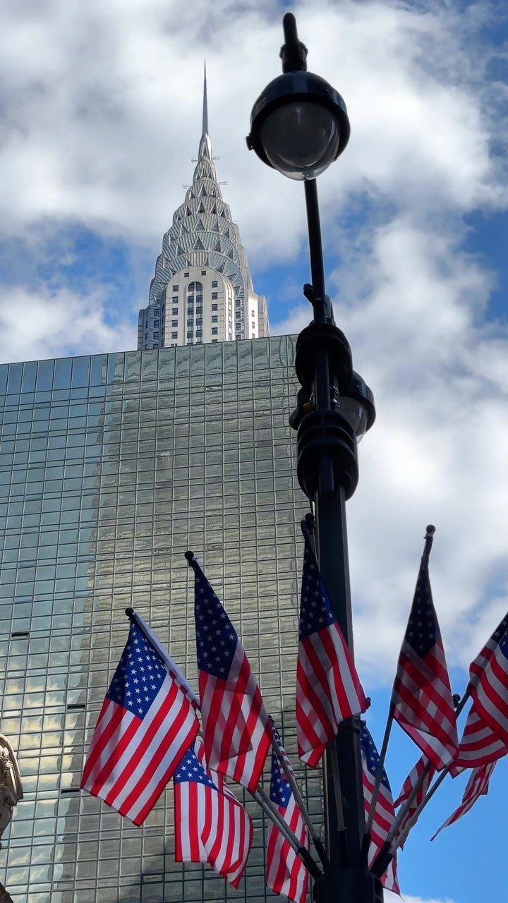 Chrysler Building and glass skyscraper with American flags and a black street lamp.