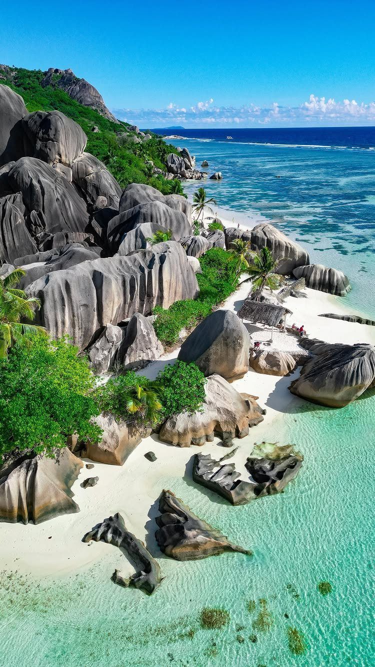 Tropical beach with smooth grey granite boulders, white sand, and turquoise ocean water.
