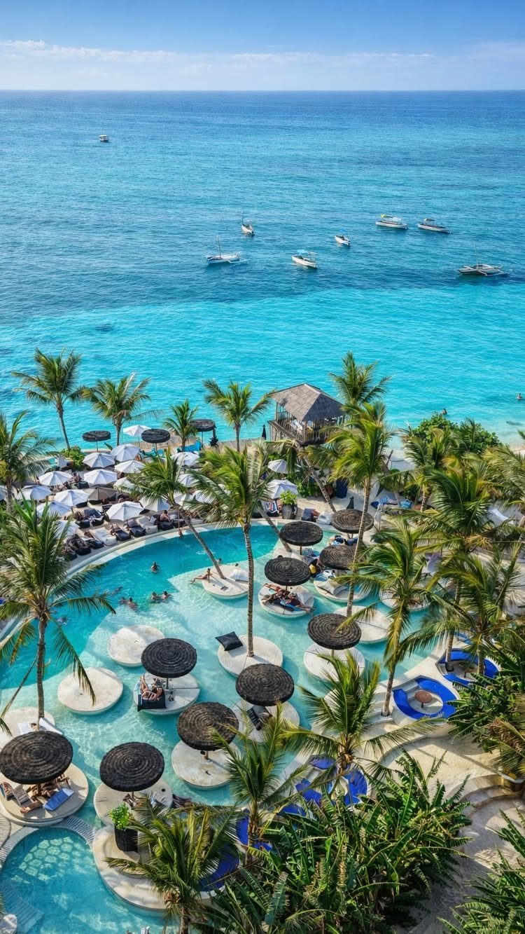 Tropical resort with a swimming pool, palm trees, and turquoise ocean water.