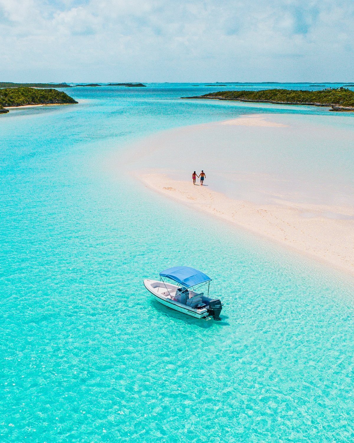 White sandbar in turquoise water with a small boat and two people walking.