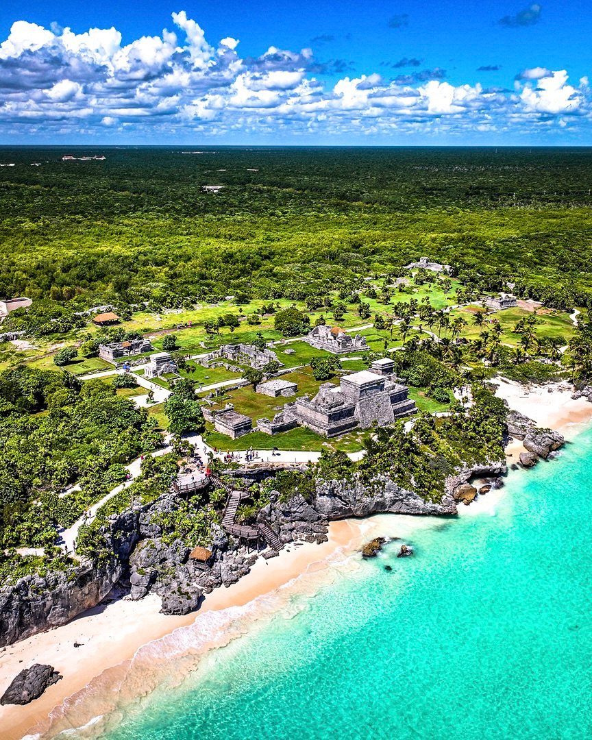 Ancient stone ruins on a tropical coastline with turquoise water and lush jungle.