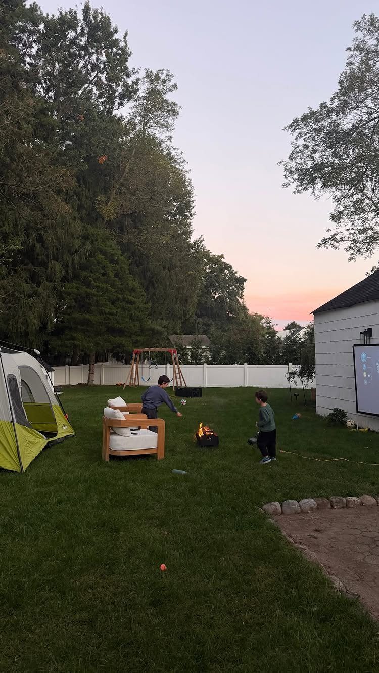 Yellow and white tent pitched in a grassy backyard with people and fire pit.