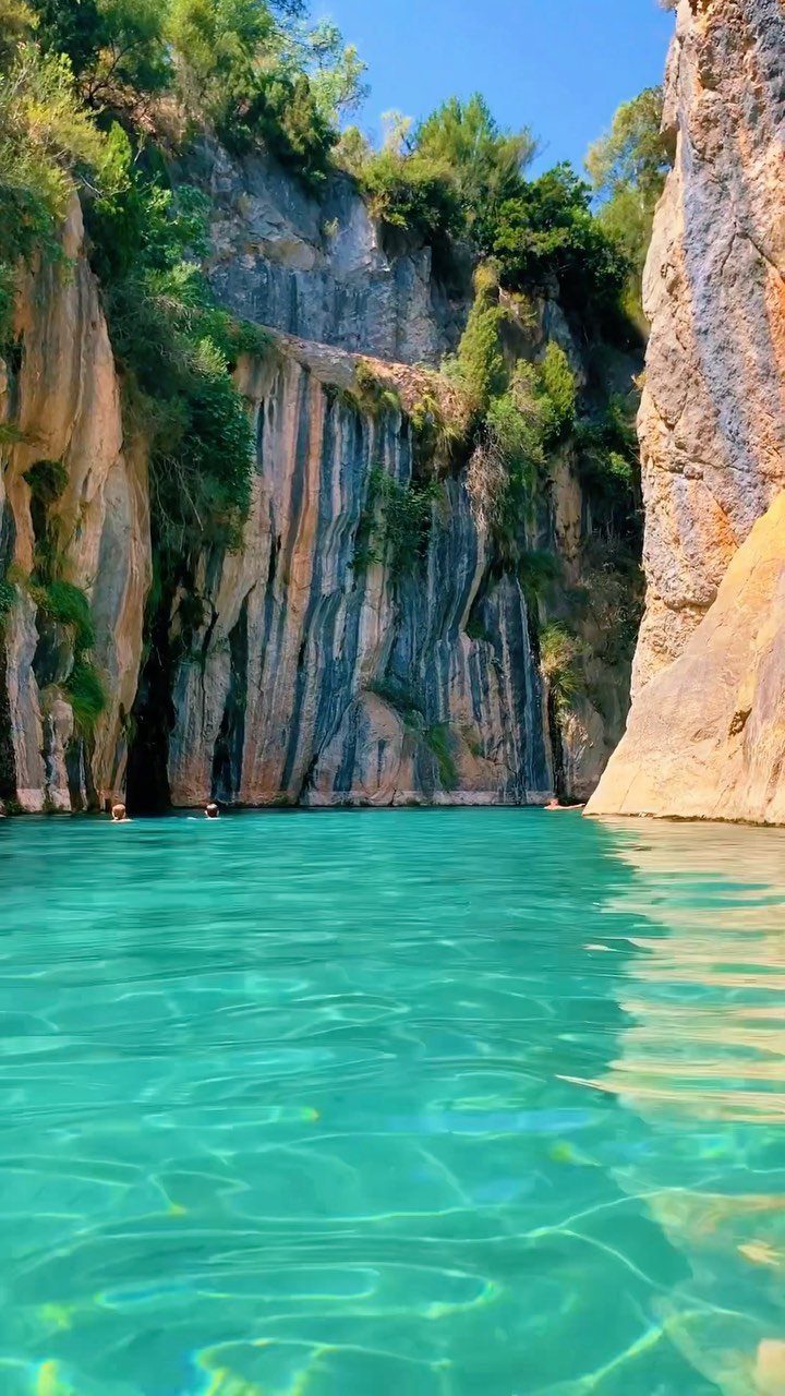 Turquoise water in a rocky canyon with green trees and steep cliffs.