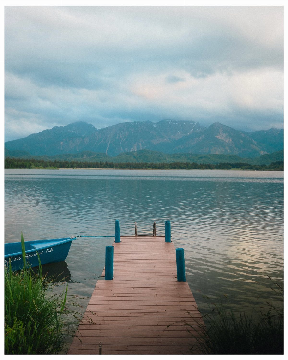 Wooden pier and blue boat on a calm lake with mountains in background