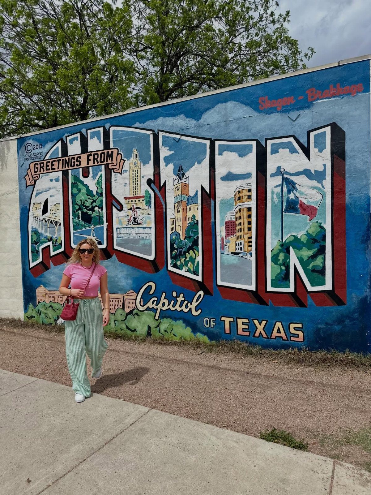 Woman standing in front of a colorful Austin, Texas greetings mural on a wall.