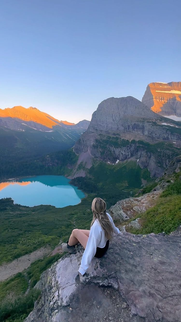 Woman sitting on a rocky cliff overlooking a turquoise lake and rugged mountains.