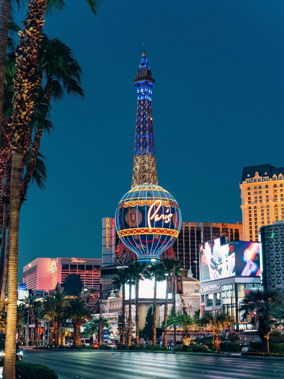 Las Vegas strip at night featuring the Eiffel Tower replica and Paris balloon.
