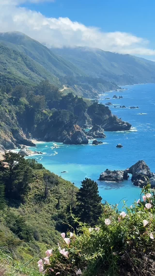 Rugged green mountains and rocky cliffs overlooking a bright blue ocean coastline.