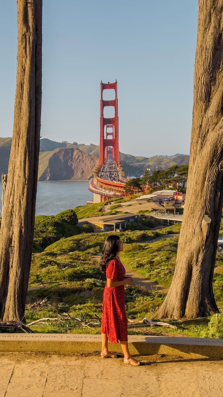 Woman in red dress looking at the Golden Gate Bridge from a hillside.