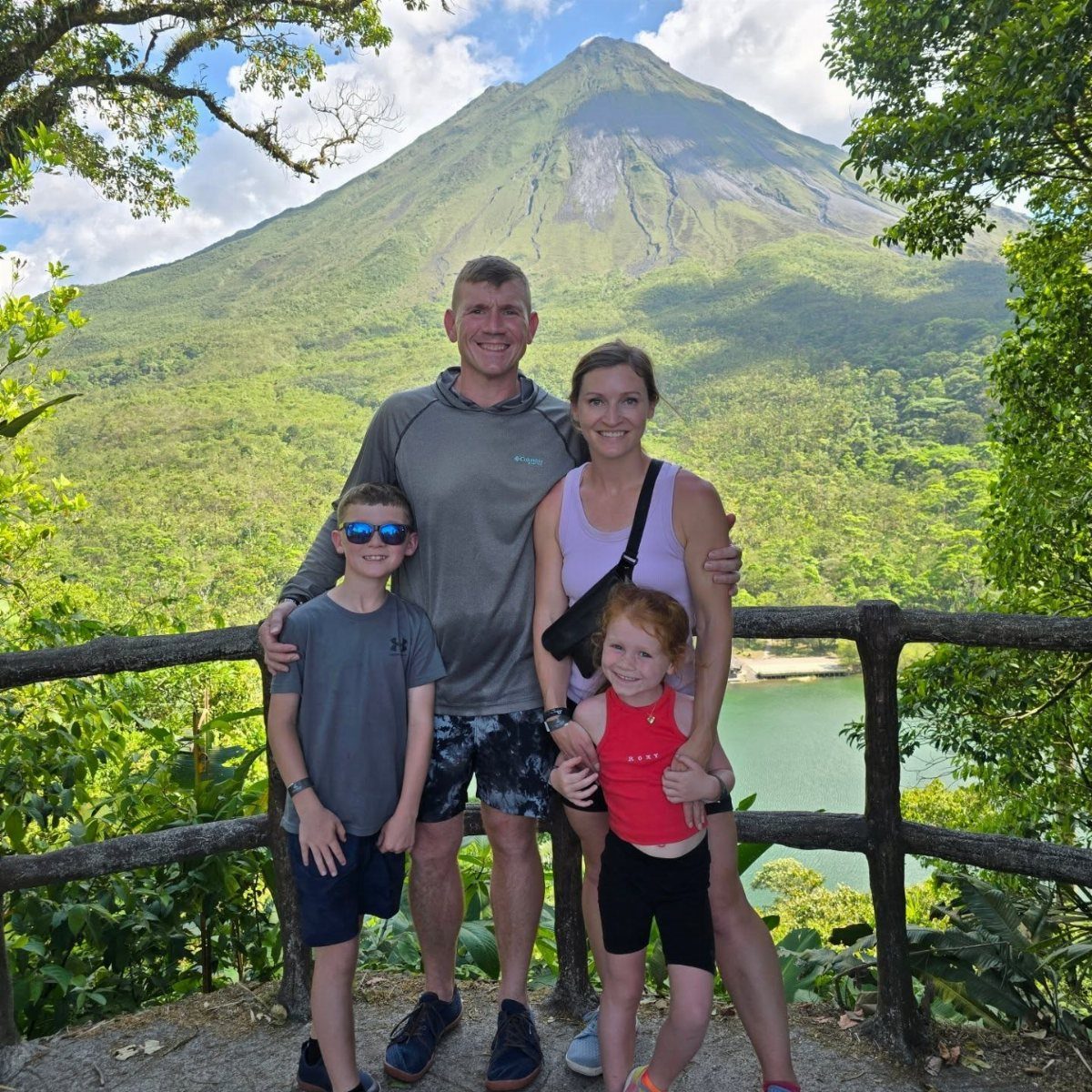 14 Places to Travel With Family: Beaches, Parks and Cities 5 Family of four posing in front of a large volcano and lush tropical landscape.