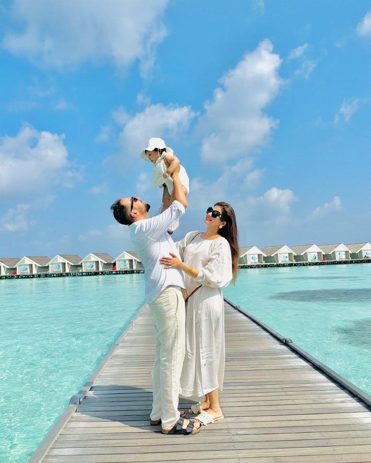 14 Places to Travel With Family: Beaches, Parks and Cities 8 Family in white clothing on a wooden pier with overwater bungalows in Maldives
